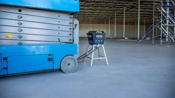 Load balancer oplaadstation van RECO aangesloten op een elektrische schaarhoogwerker in een bedrijfshal