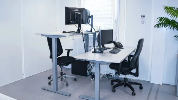 Verstelbare zit-sta-bureaus met bureaustoelen en beeldschermen in een tijdelijke kantoorruimte.