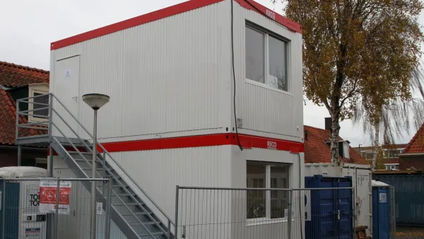 Gestapelde RECO bouwunits met buitentrap op een bouwlocatie.